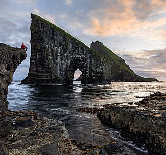 Tourist looking the Drangarnir rocks, a collective name of two sea stacks, which are called Stri Drangur (large rock) and Ltli Drangur (small rock) respectively, and are located next to each other between the islands of Vgar and Tindhlmur, Srvgsfjrur Fjord near Srvgur, Faeroe islands, Denmark